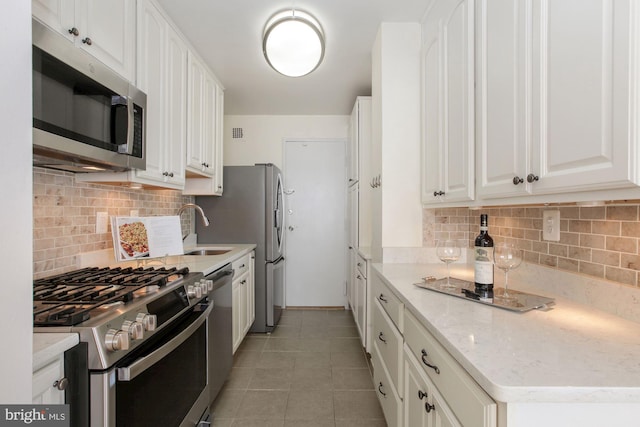 kitchen featuring light tile patterned floors, backsplash, stainless steel appliances, light stone countertops, and white cabinets