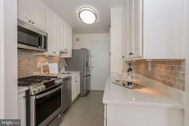 kitchen with sink, white cabinetry, light stone counters, light tile patterned floors, and appliances with stainless steel finishes