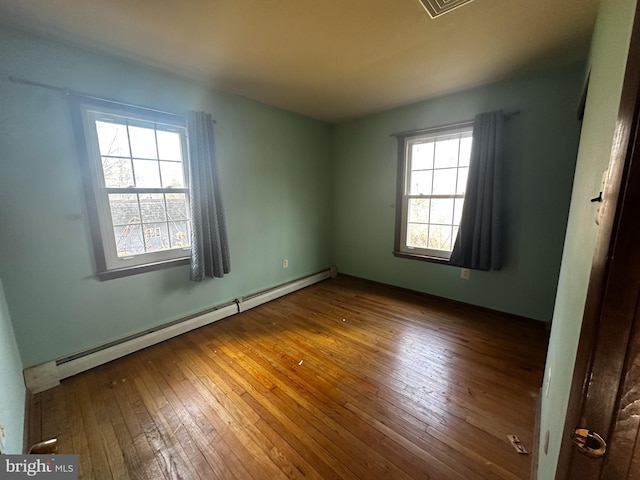 unfurnished room featuring hardwood / wood-style flooring and a baseboard heating unit