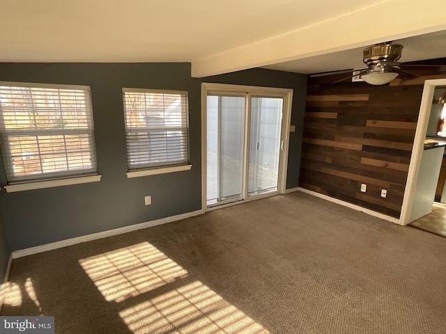 carpeted empty room featuring wooden walls and ceiling fan