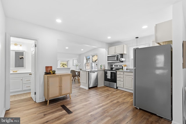 kitchen featuring pendant lighting, white cabinets, hardwood / wood-style flooring, kitchen peninsula, and stainless steel appliances