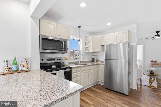 kitchen with sink, hanging light fixtures, light stone counters, stainless steel appliances, and light wood-type flooring