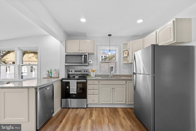 kitchen with sink, appliances with stainless steel finishes, hardwood / wood-style floors, hanging light fixtures, and light stone countertops