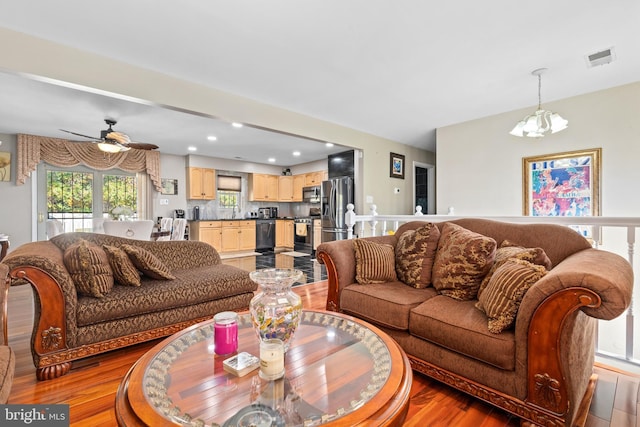 living room featuring ceiling fan with notable chandelier and light hardwood / wood-style flooring