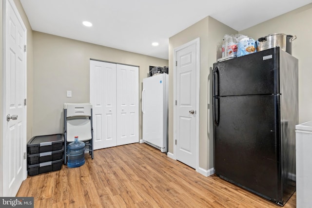 kitchen featuring black fridge, white fridge, and light hardwood / wood-style flooring