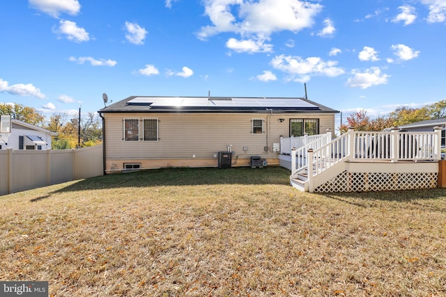 back of property with a wooden deck, a yard, solar panels, and central air condition unit