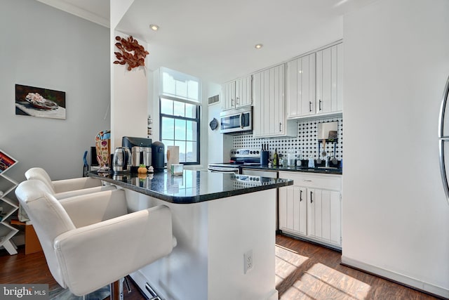 kitchen featuring a kitchen breakfast bar, stainless steel appliances, kitchen peninsula, and white cabinets