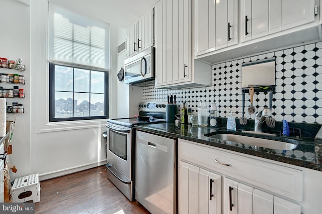 kitchen with white cabinetry, appliances with stainless steel finishes, sink, and dark stone countertops