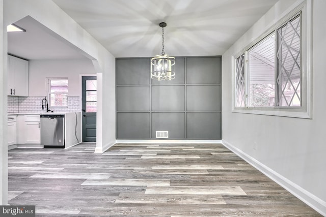 unfurnished dining area featuring sink, a notable chandelier, and light wood-type flooring