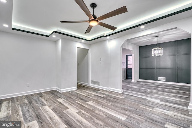 spare room with wood-type flooring, a raised ceiling, and ceiling fan with notable chandelier