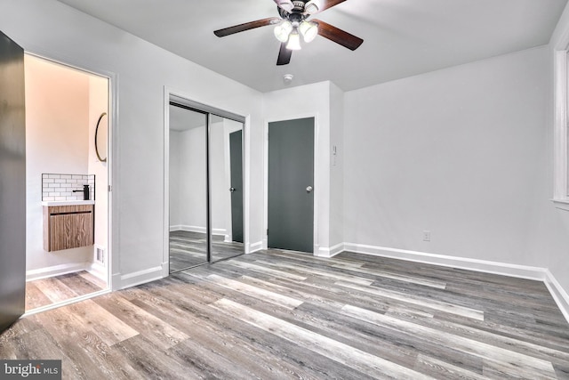 unfurnished bedroom with wood-type flooring, ceiling fan, ensuite bath, and a closet