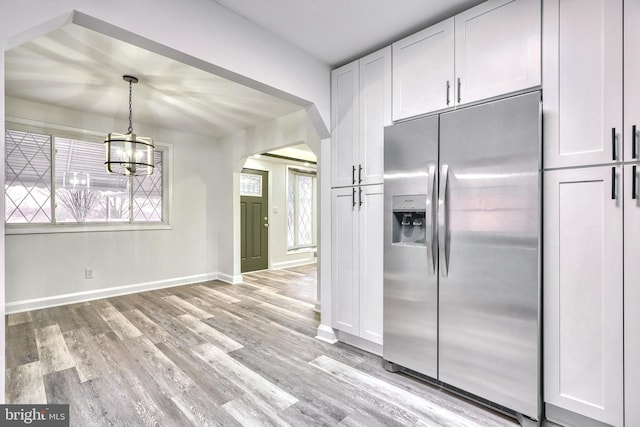 kitchen featuring white cabinetry, light wood-type flooring, stainless steel fridge, hanging light fixtures, and an inviting chandelier