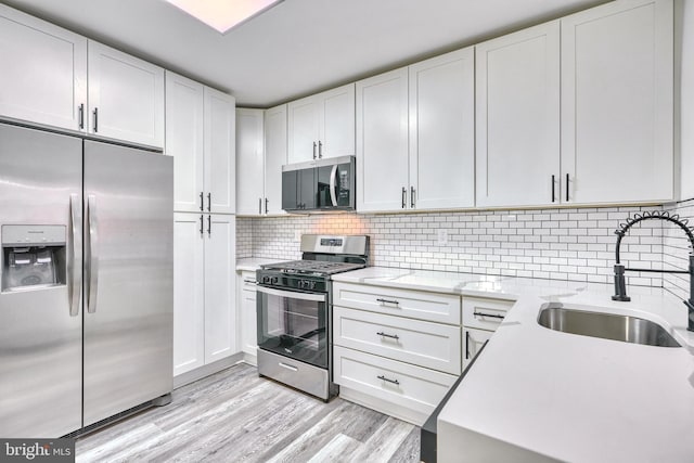 kitchen with sink, appliances with stainless steel finishes, light stone countertops, white cabinets, and light wood-type flooring