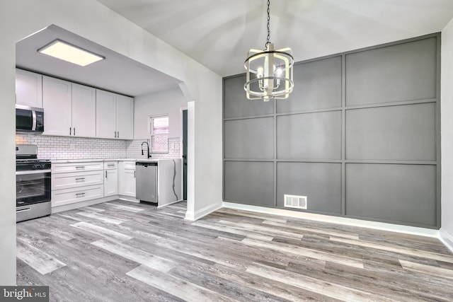 kitchen with white cabinetry, stainless steel appliances, light hardwood / wood-style floors, and backsplash