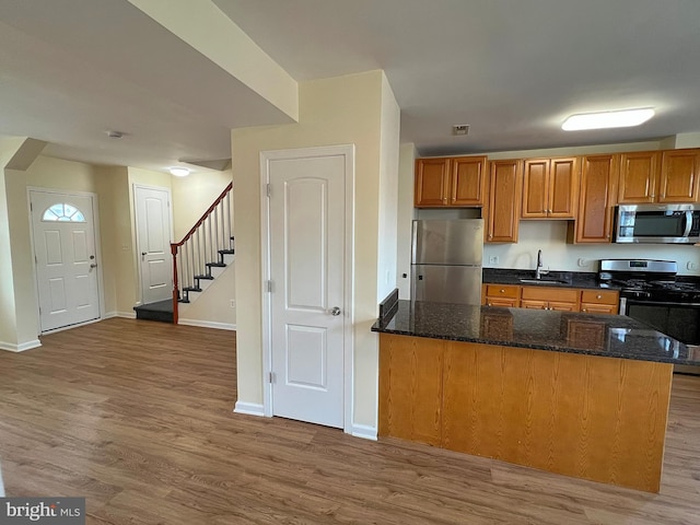 kitchen featuring stainless steel appliances, wood-type flooring, sink, and dark stone countertops