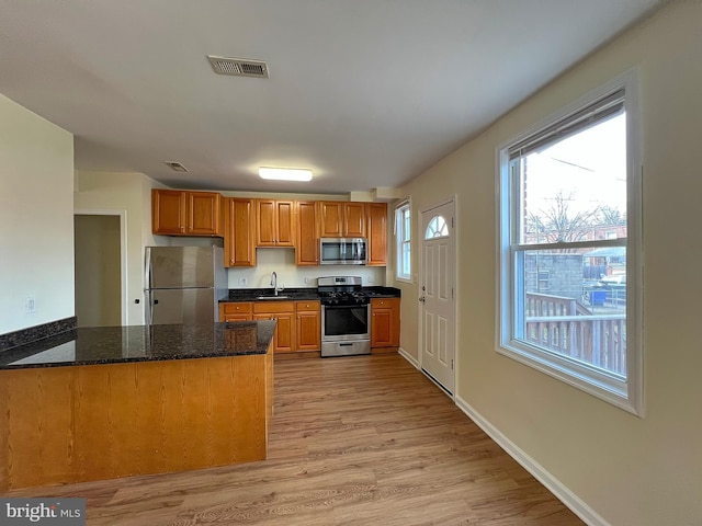 kitchen with sink, appliances with stainless steel finishes, light hardwood / wood-style floors, kitchen peninsula, and dark stone counters