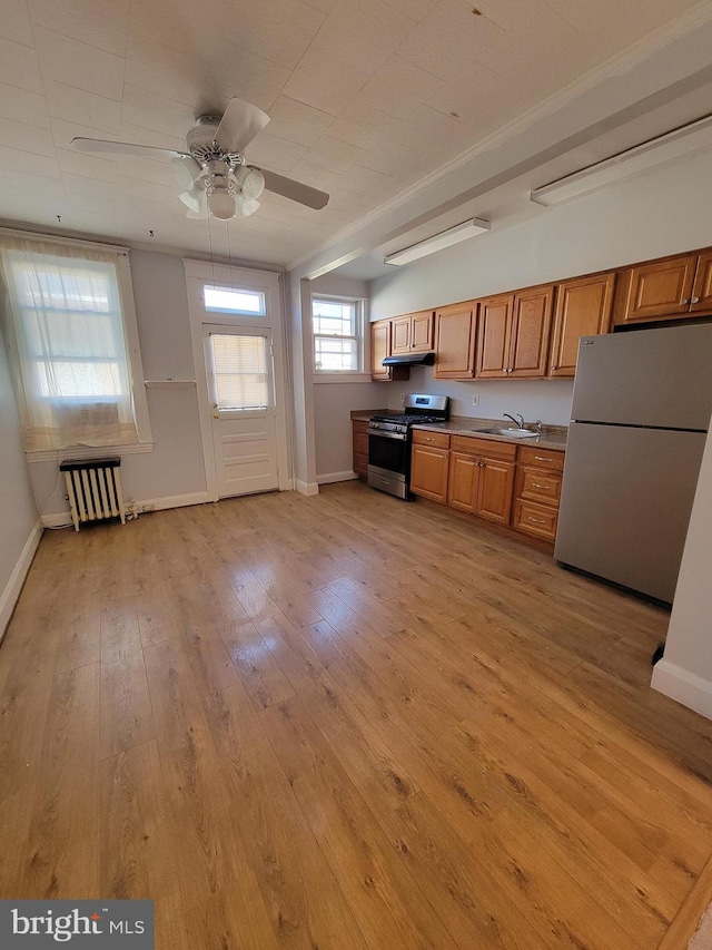 kitchen featuring appliances with stainless steel finishes, radiator, sink, ceiling fan, and light hardwood / wood-style floors