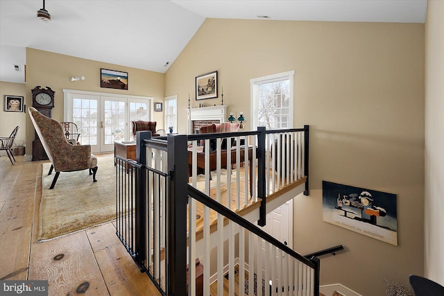 stairway featuring a brick fireplace, a healthy amount of sunlight, high vaulted ceiling, and french doors