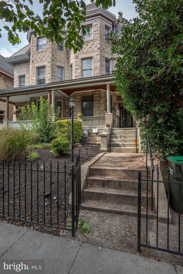 view of property featuring stone siding, a fenced front yard, and covered porch