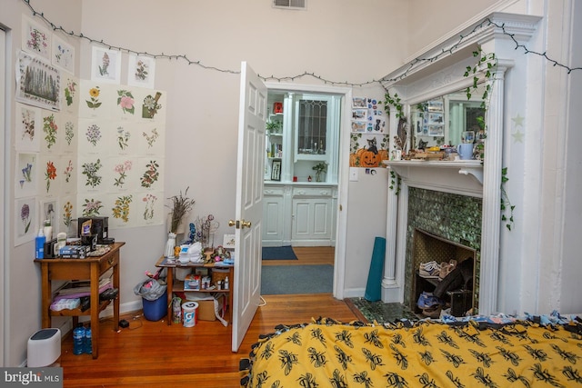 bedroom with visible vents, baseboards, a tiled fireplace, and wood finished floors