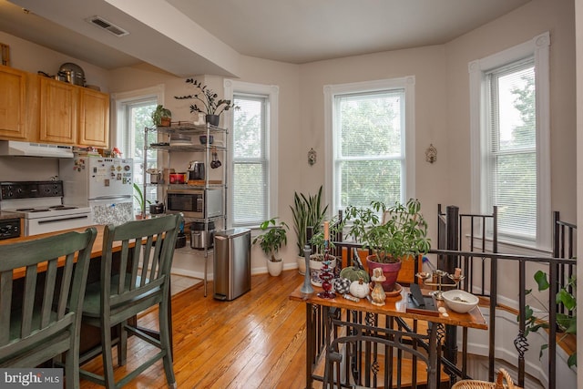 kitchen with white appliances, visible vents, under cabinet range hood, light wood-style flooring, and baseboards