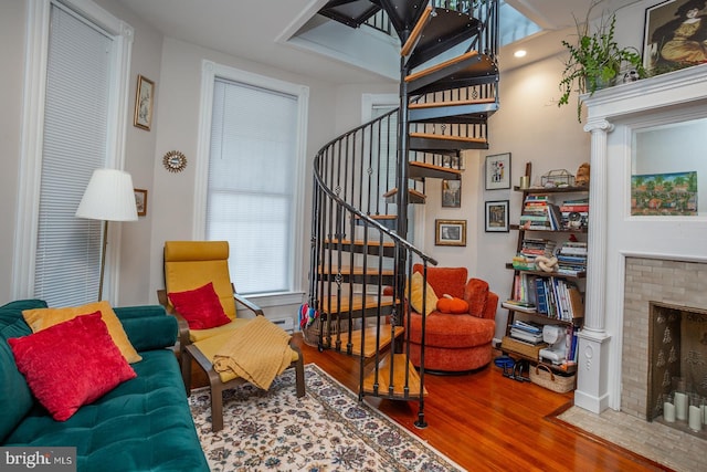 sitting room with stairway, a brick fireplace, and wood finished floors