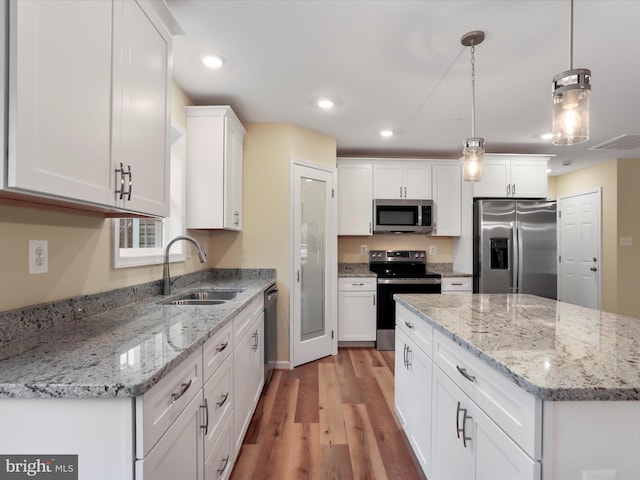 kitchen featuring pendant lighting, sink, appliances with stainless steel finishes, light stone countertops, and white cabinets