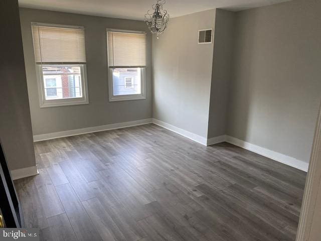 spare room with a notable chandelier and dark wood-type flooring