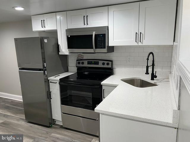 kitchen with sink, stainless steel appliances, tasteful backsplash, light hardwood / wood-style floors, and white cabinets