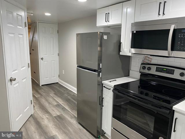 kitchen featuring tasteful backsplash, hardwood / wood-style floors, white cabinets, and appliances with stainless steel finishes