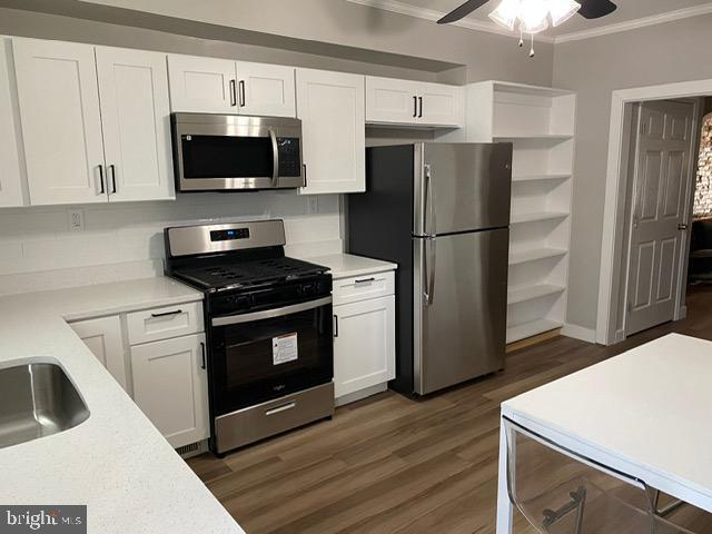 kitchen featuring dark wood-type flooring, ceiling fan, white cabinetry, stainless steel appliances, and ornamental molding