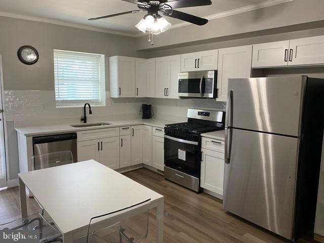 kitchen with ornamental molding, appliances with stainless steel finishes, sink, and white cabinets