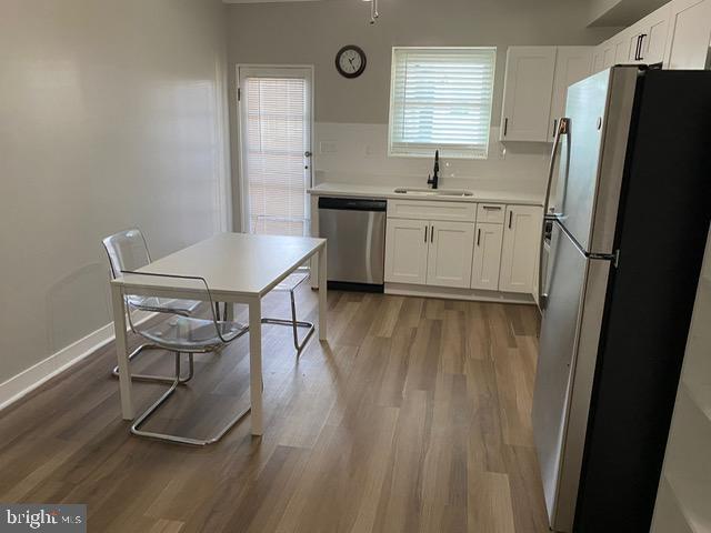 kitchen with appliances with stainless steel finishes, sink, white cabinets, and light hardwood / wood-style flooring