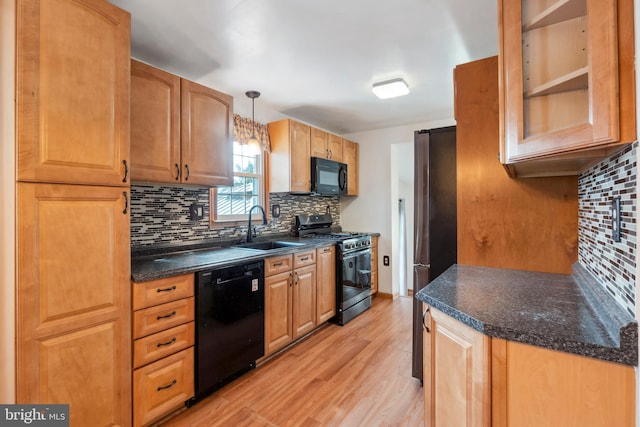 kitchen with glass insert cabinets, decorative light fixtures, light wood-type flooring, black appliances, and a sink