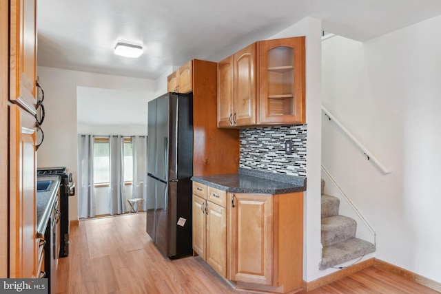 kitchen featuring backsplash, freestanding refrigerator, light wood finished floors, dark countertops, and glass insert cabinets