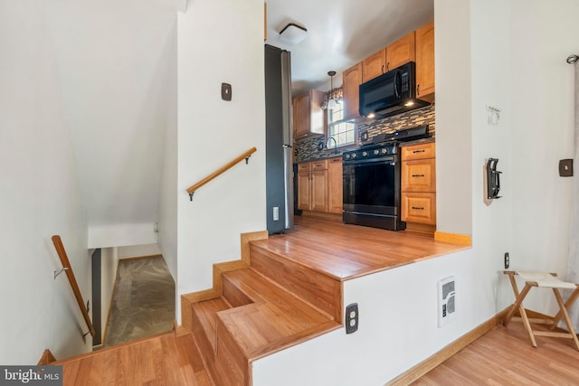 kitchen with decorative light fixtures, dark countertops, decorative backsplash, appliances with stainless steel finishes, and light wood-style floors