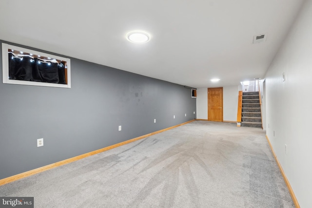 finished below grade area featuring baseboards, stairway, visible vents, and light colored carpet