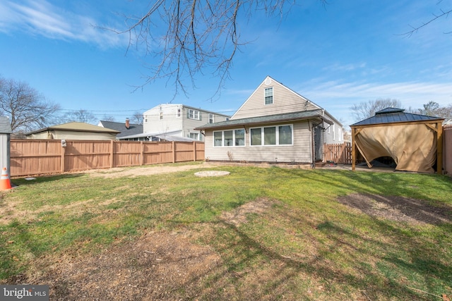 rear view of house with a fenced backyard, a lawn, and a gazebo