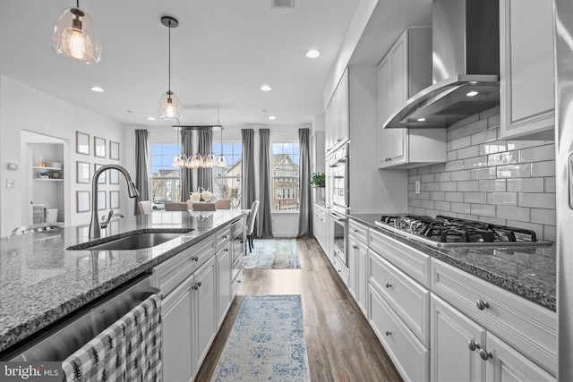 kitchen with white cabinets, appliances with stainless steel finishes, sink, and wall chimney range hood