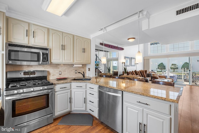 kitchen with sink, appliances with stainless steel finishes, hanging light fixtures, kitchen peninsula, and light wood-type flooring