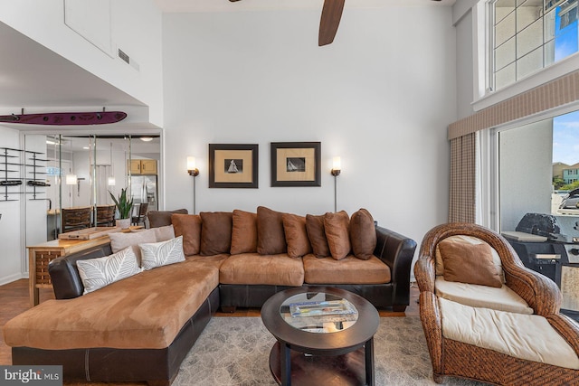 living room with hardwood / wood-style flooring, ceiling fan, beamed ceiling, and a high ceiling