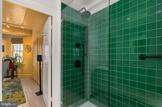 bathroom with wood-type flooring, rail lighting, and a tile shower