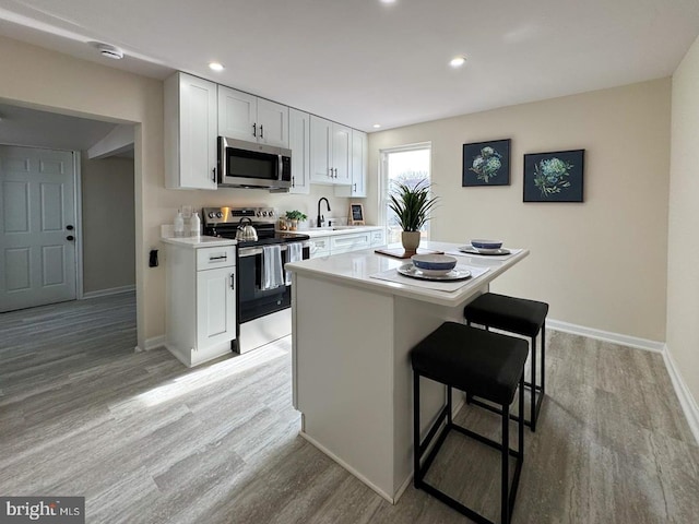 kitchen with a kitchen breakfast bar, stainless steel appliances, a center island, white cabinets, and light wood-type flooring