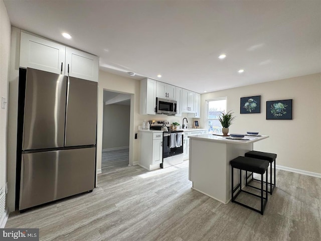 kitchen featuring a kitchen island, appliances with stainless steel finishes, a breakfast bar area, white cabinets, and light hardwood / wood-style flooring