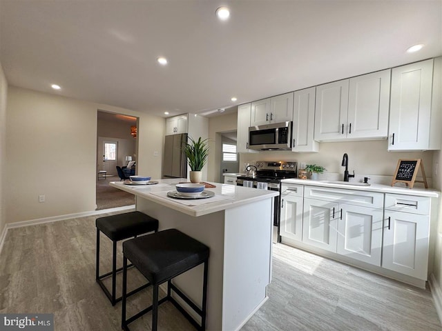 kitchen featuring sink, light hardwood / wood-style flooring, white cabinetry, stainless steel appliances, and a center island