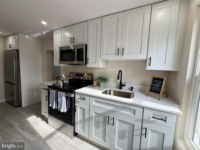 kitchen with sink, white cabinetry, light stone counters, light wood-type flooring, and appliances with stainless steel finishes