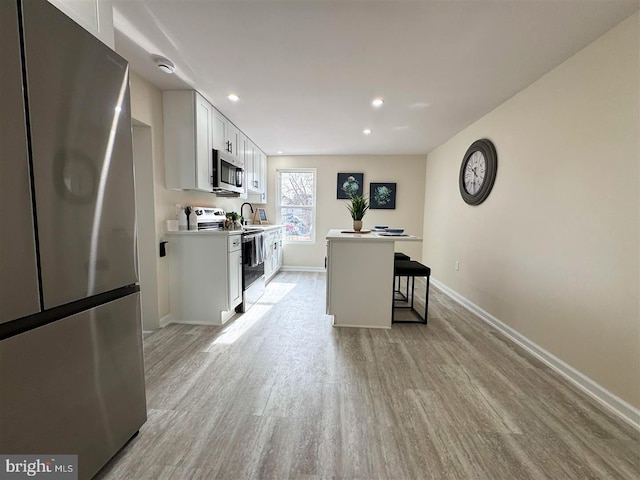 kitchen with light hardwood / wood-style flooring, a breakfast bar area, stainless steel appliances, a center island, and white cabinets