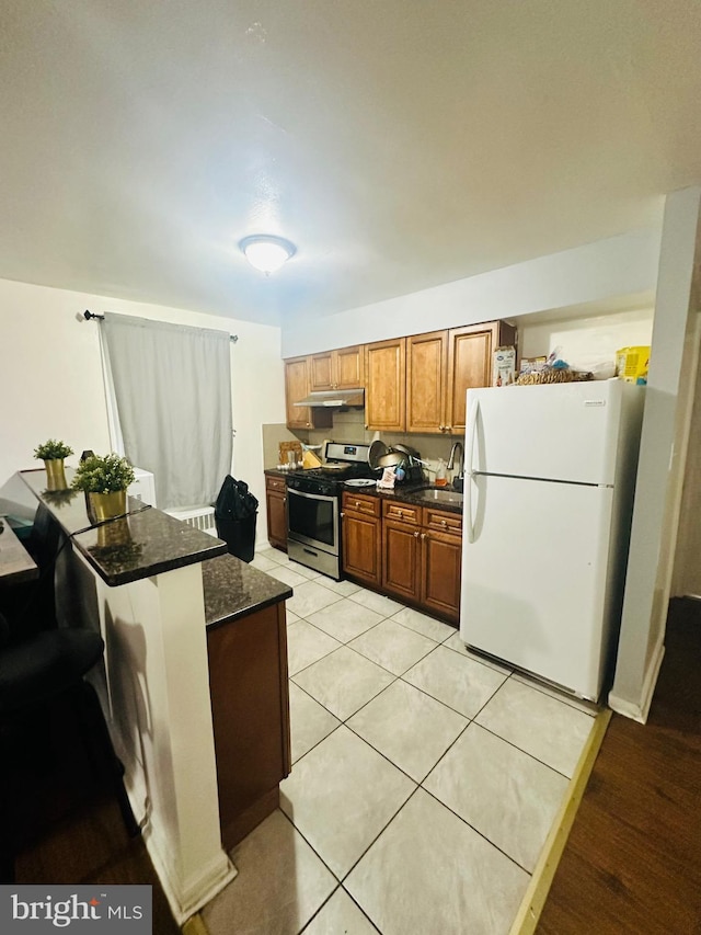 kitchen with sink, stainless steel range with gas stovetop, white refrigerator, light tile patterned flooring, and dark stone counters