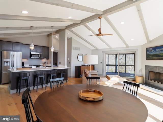 dining space featuring a fireplace, visible vents, a ceiling fan, light wood-style floors, and beamed ceiling