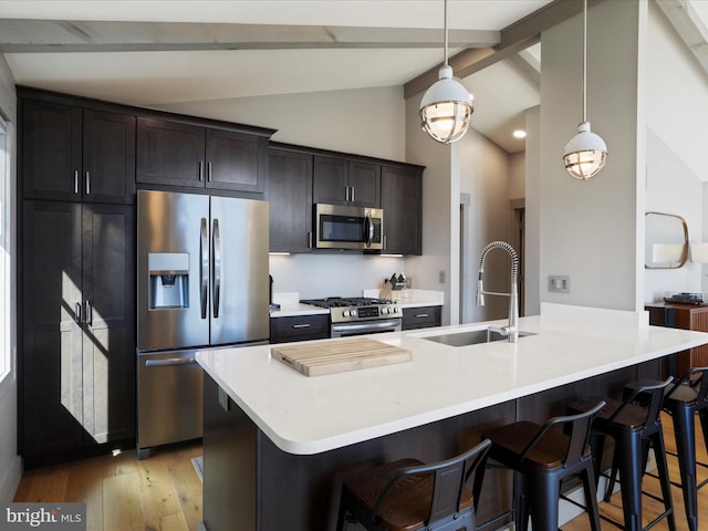 kitchen featuring appliances with stainless steel finishes, a sink, light wood-style floors, and a kitchen breakfast bar